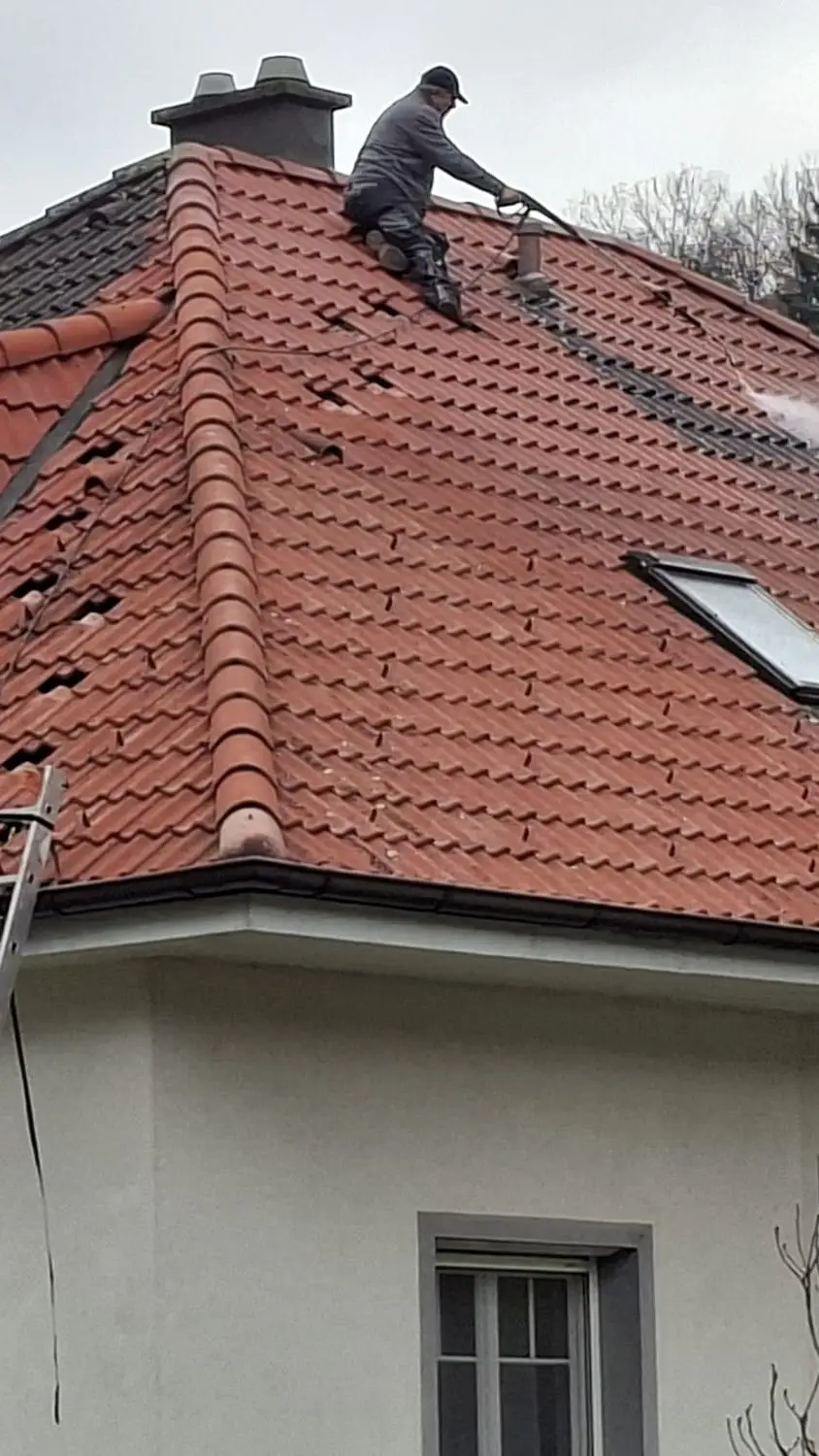 Dachreinigung mit Hochdruck auf einem roten Ziegeldach, unten Leiter und Reinigungsgerät